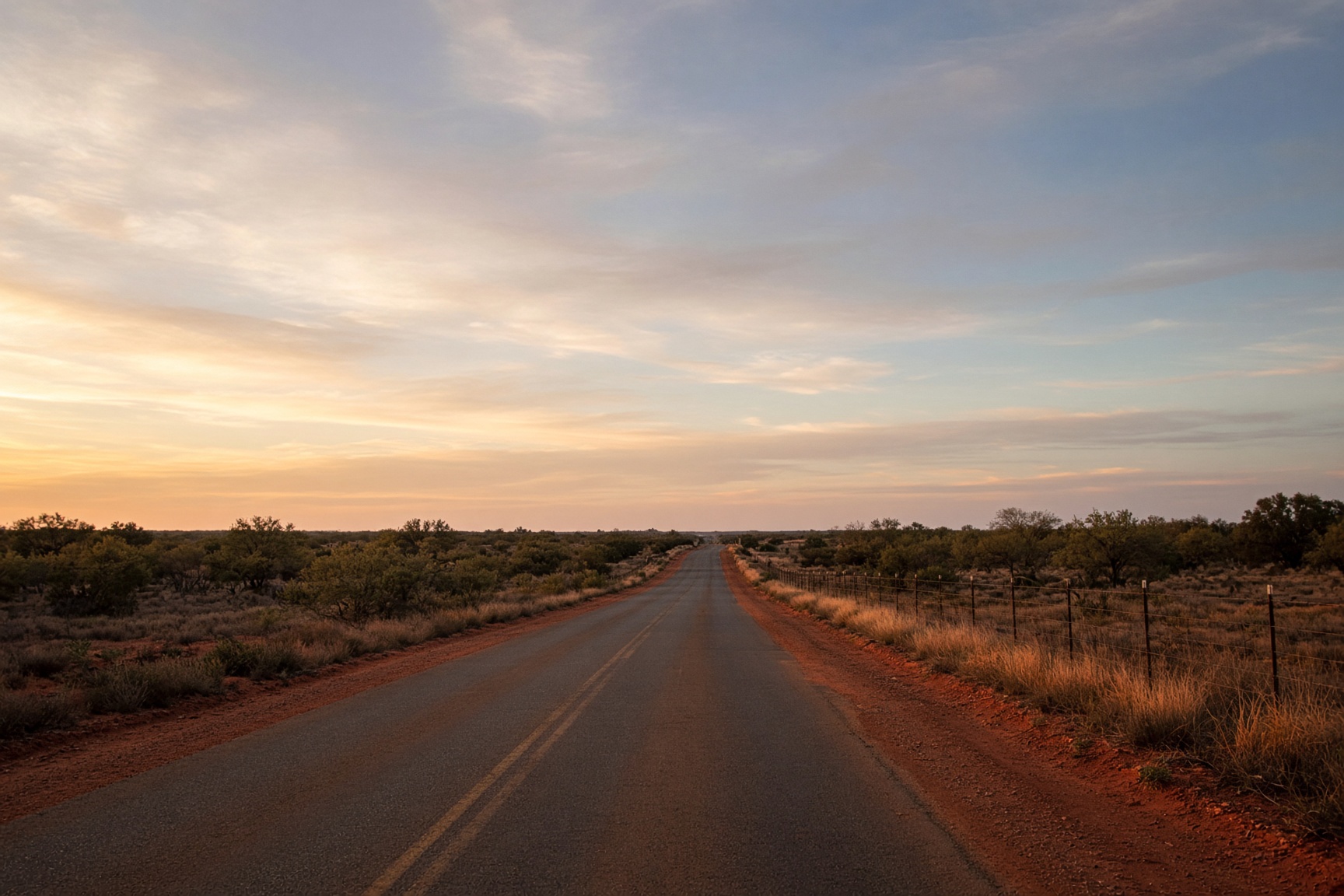 An empty two-lane Texas ranch road at golden hour